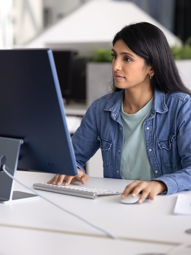 Woman using a desktop computer with keyboard and mouse at a white desk in an office